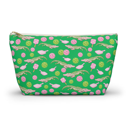 A green zippered cosmetic pouch featuring a repeating pattern of pink and green alligators, Pickleballs, and paddles shapes, shown on a white background.